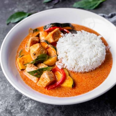 square image thai red curry chicken with squash, bell peppers, and rice in a white bowl
