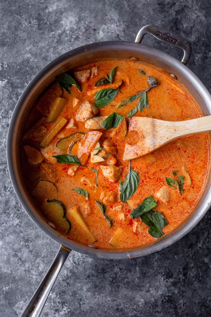 saute pan with thai red curry including chicken, squash, bell peppers and a wooden spoon