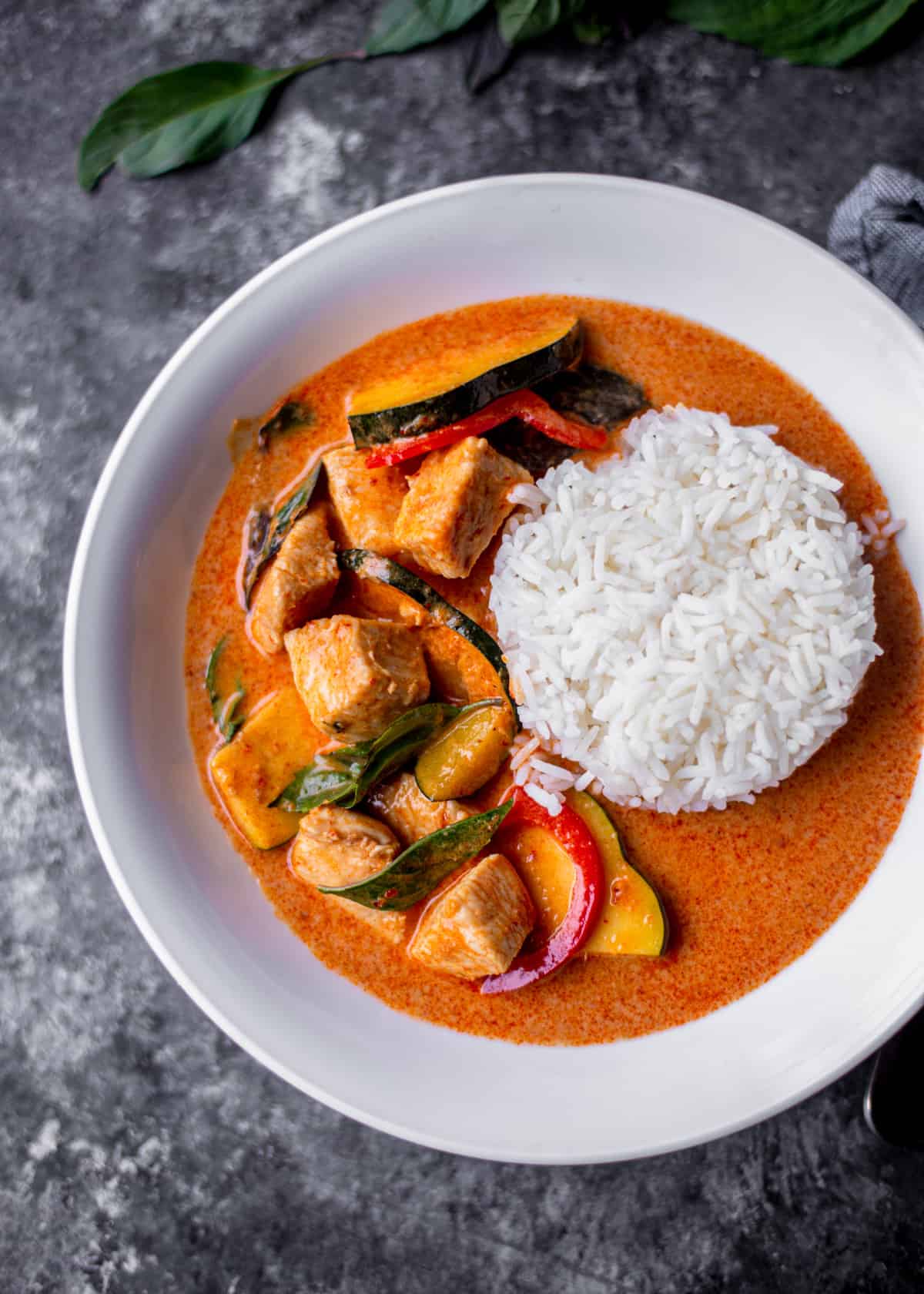 overhead image of thai red curry with chicken, squash, basil, and red peppers in a white bowl