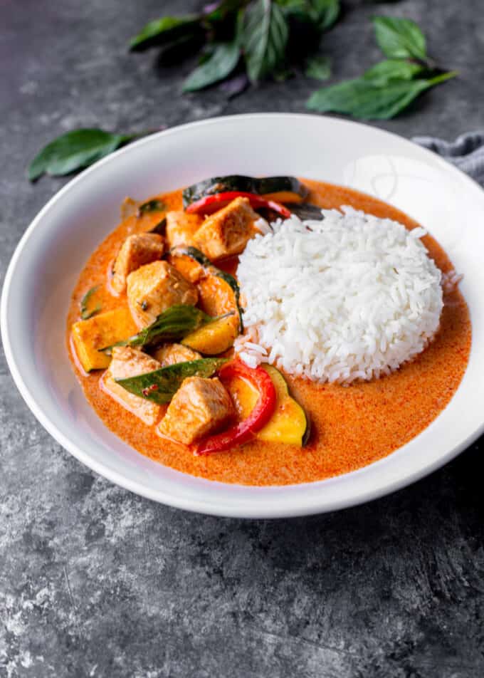 thai red curry chicken with squash, bell peppers, and rice in a white bowl