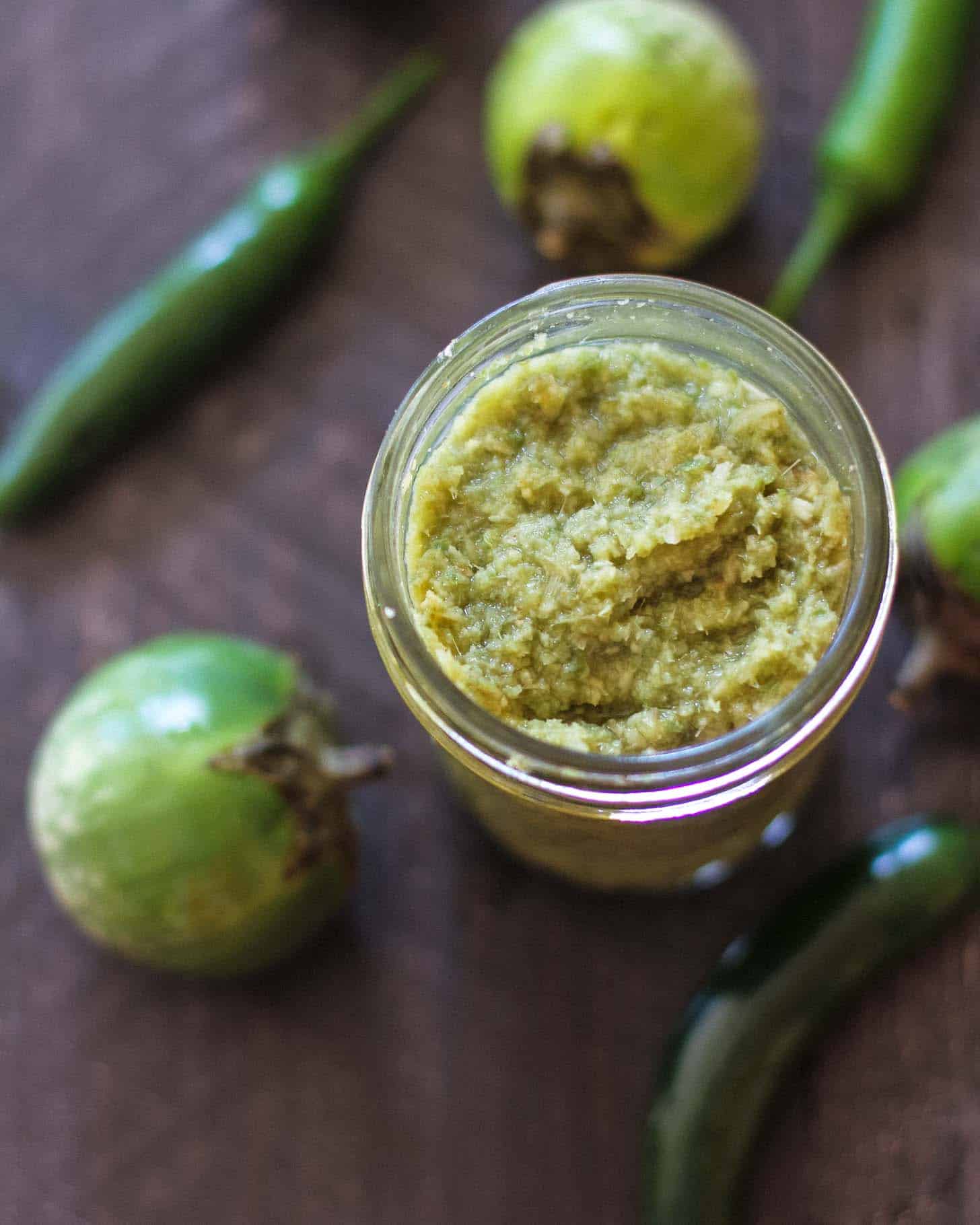 overhead image of Green curry paste in a small mason jar next to peppers 