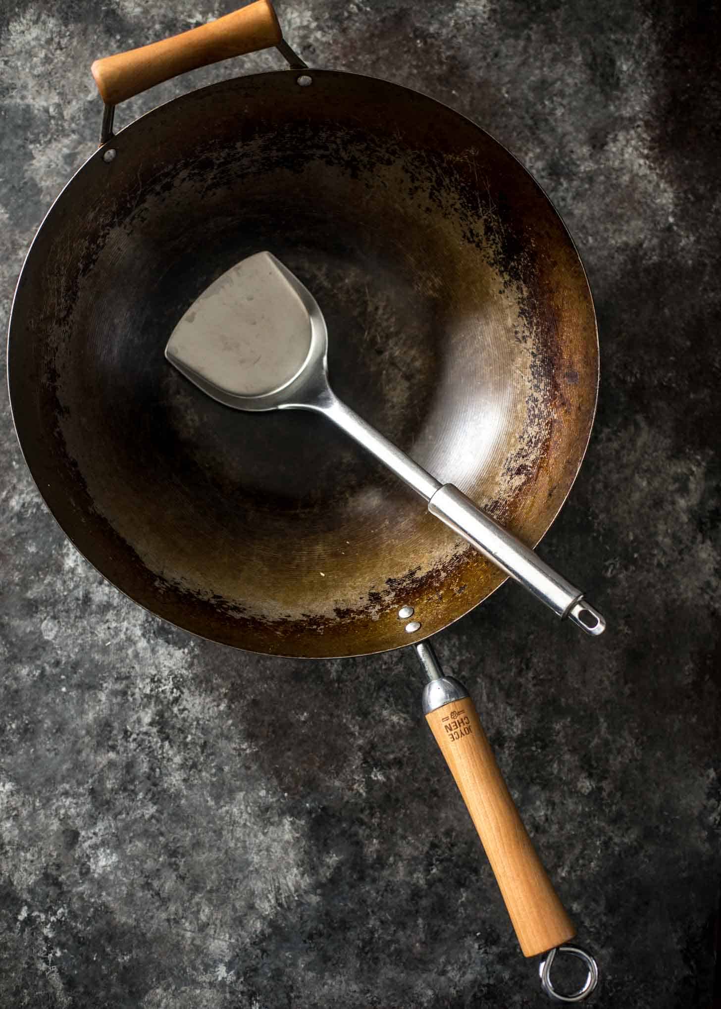 a wok and a spatula on a grey countertop