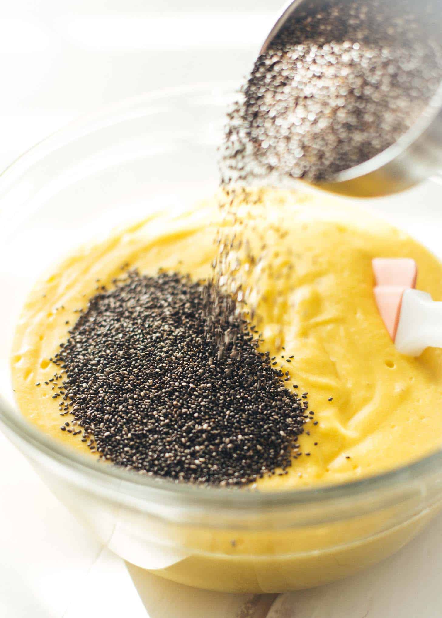 adding chia seeds to mango mix in a clear glass mixing bowl