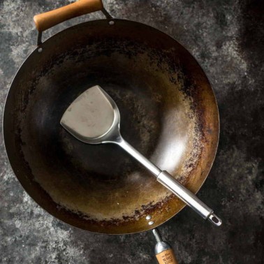 a wok with a spatula on a grey countertop