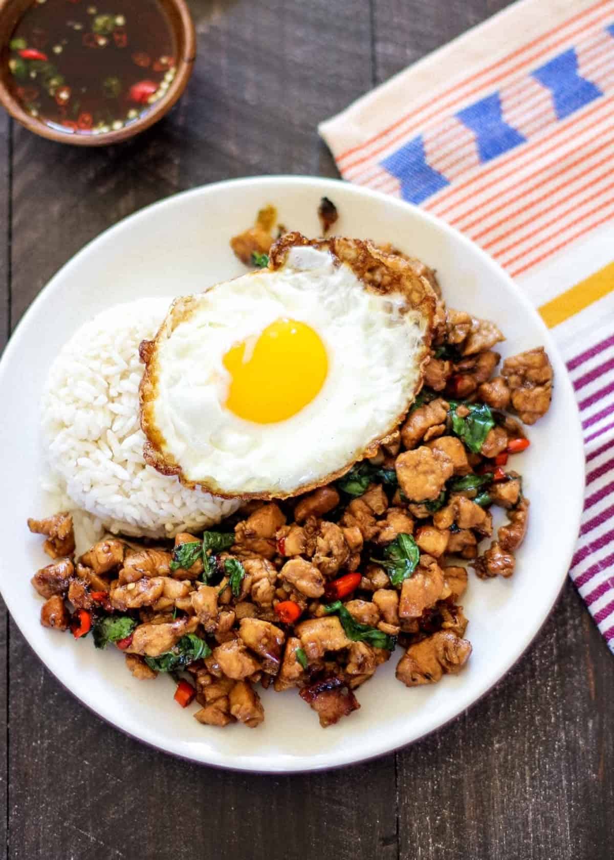 thai basil chicken topped with a fried egg on a white plate