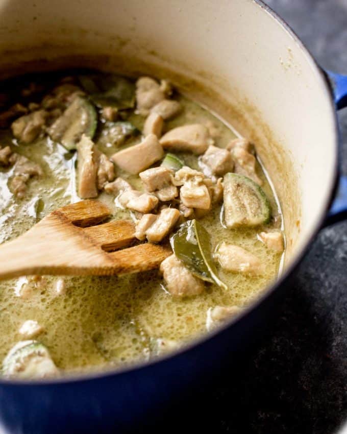 stirring thai green curry in a blue dutch oven with a wooden spoon 