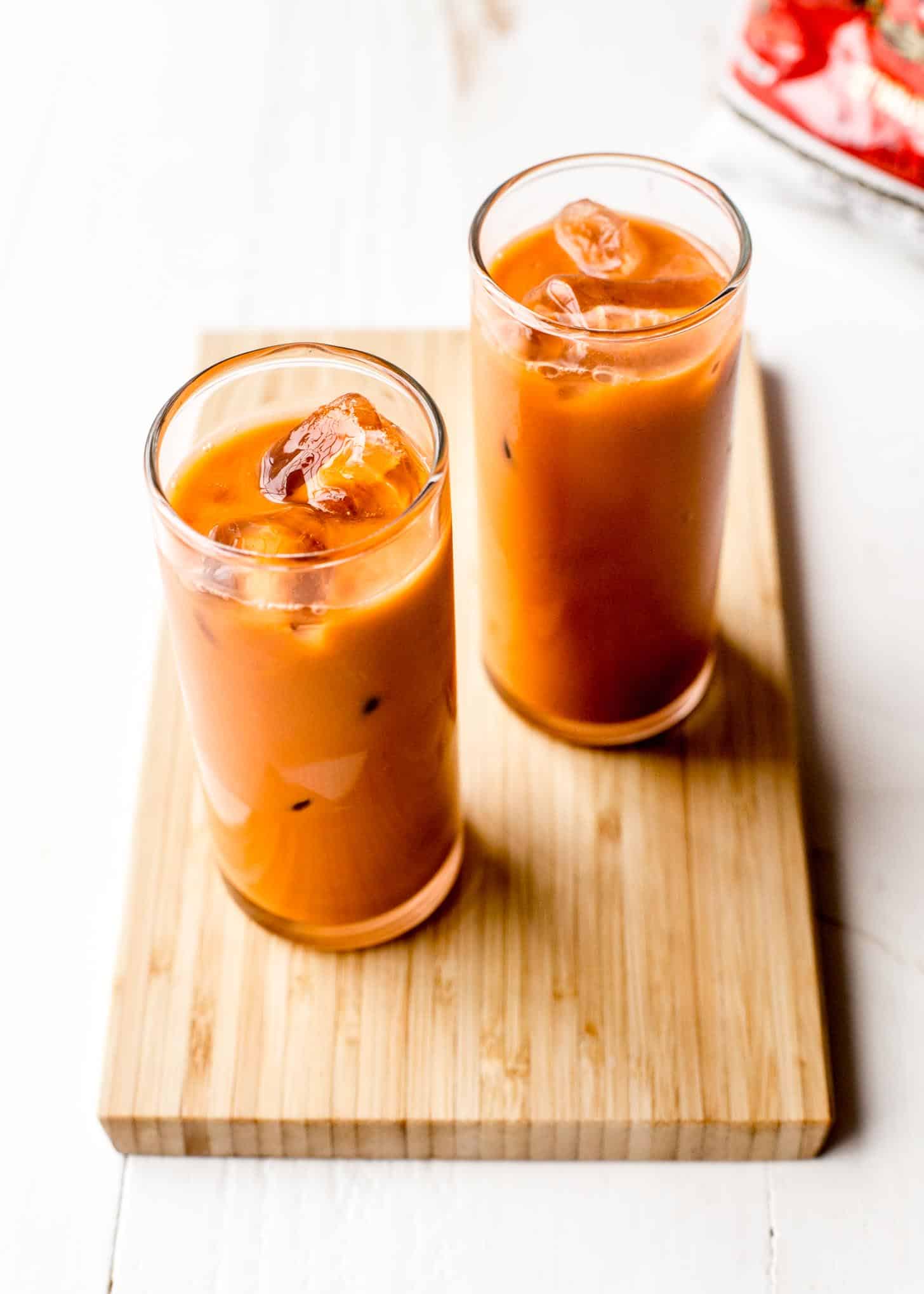 2 glasses of thai iced tea on a wooden board
