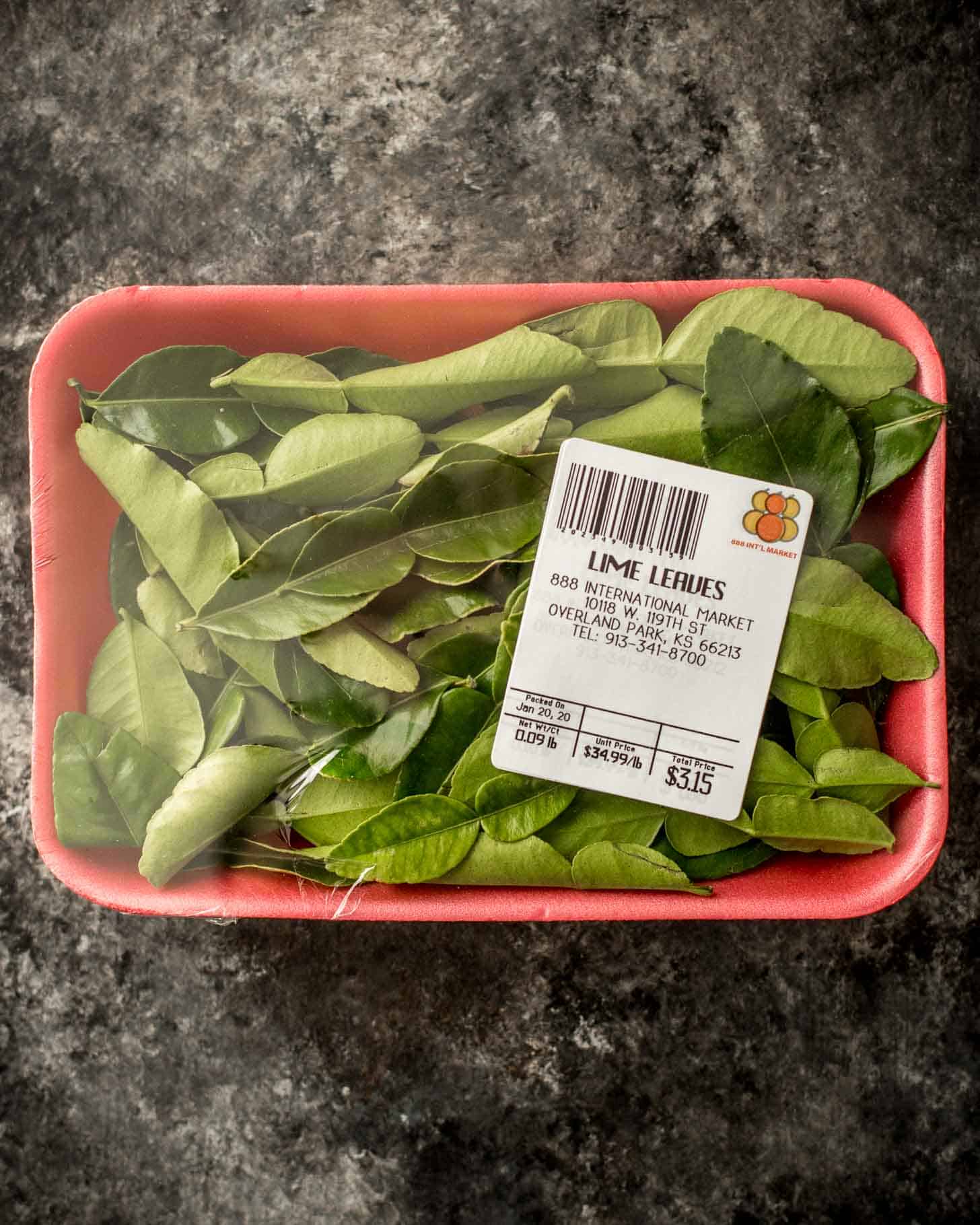 overhead image of kaffir lime leaves in a package on a grey countertop