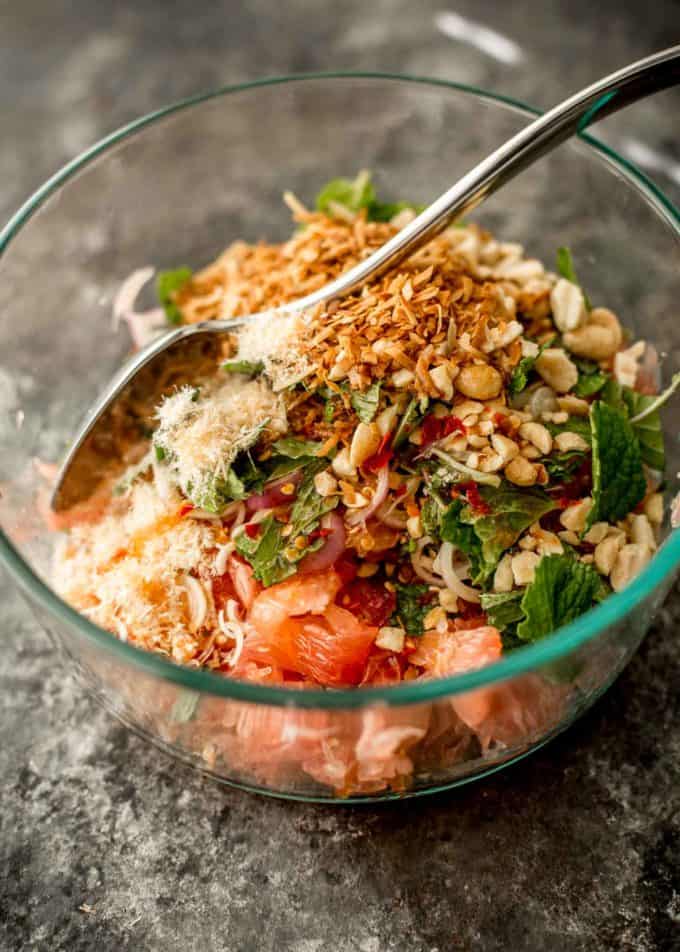 stirring thai pomelo salad in a glass bowl