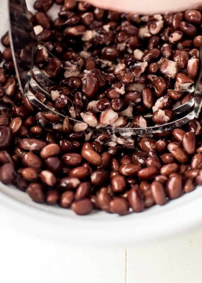 mashing black beans in a white bowl