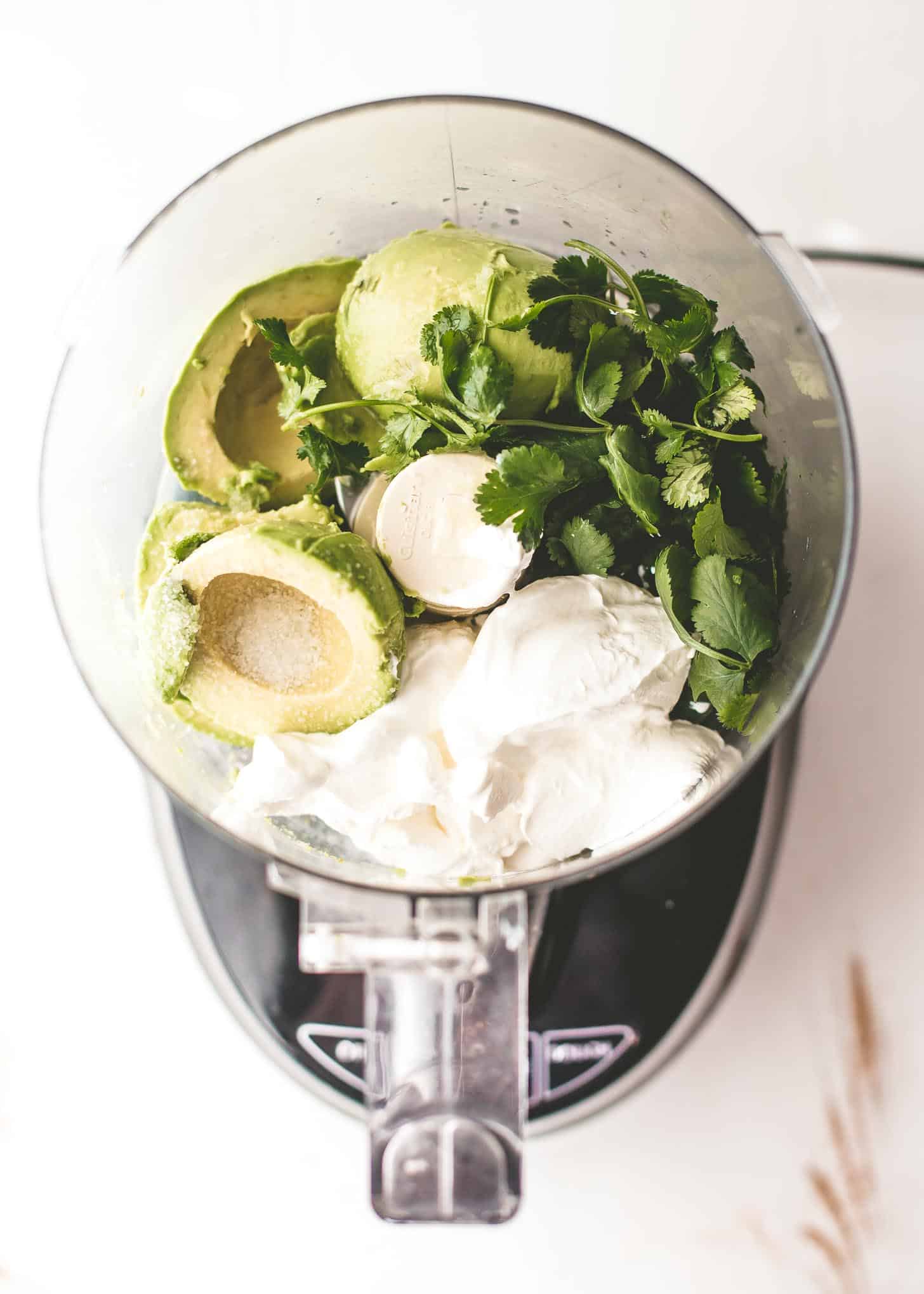 overhead image of avocado, cilantro, sour cream in a food processor