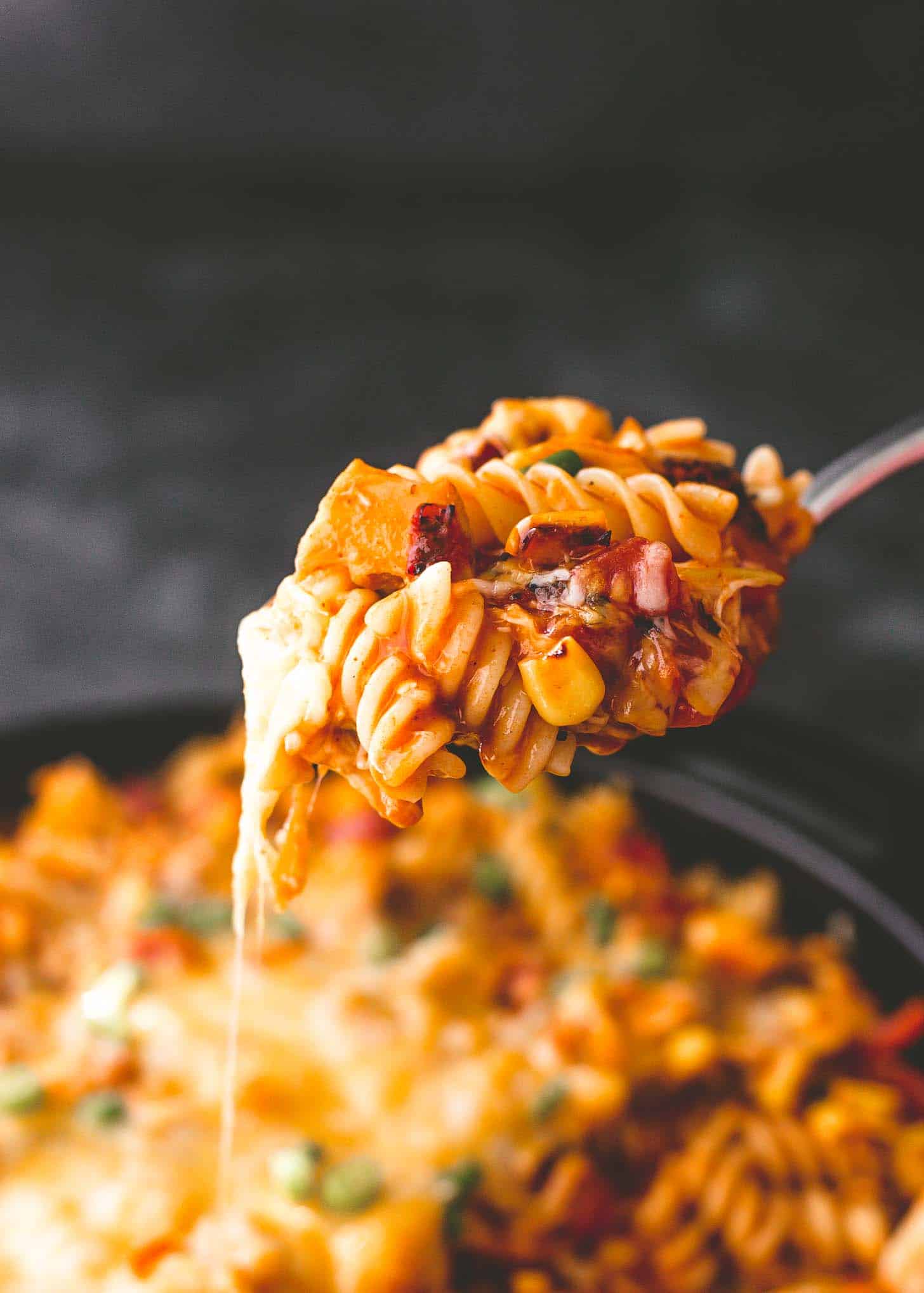 a spoonful of chicken enchilada pasta above a skillet full of casserole