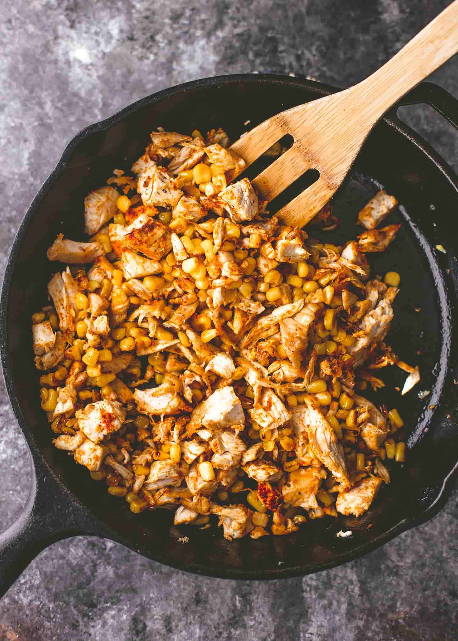 stirring chicken and corn in a cast iron skillet