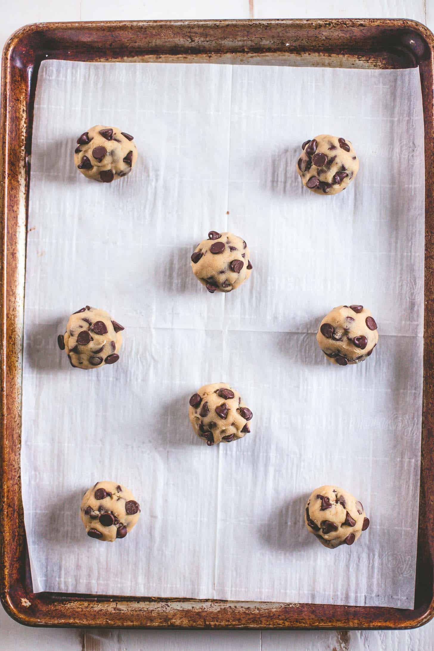 overhead image of chocolate chip cookie dough in balls on a parchment lined cookie sheet