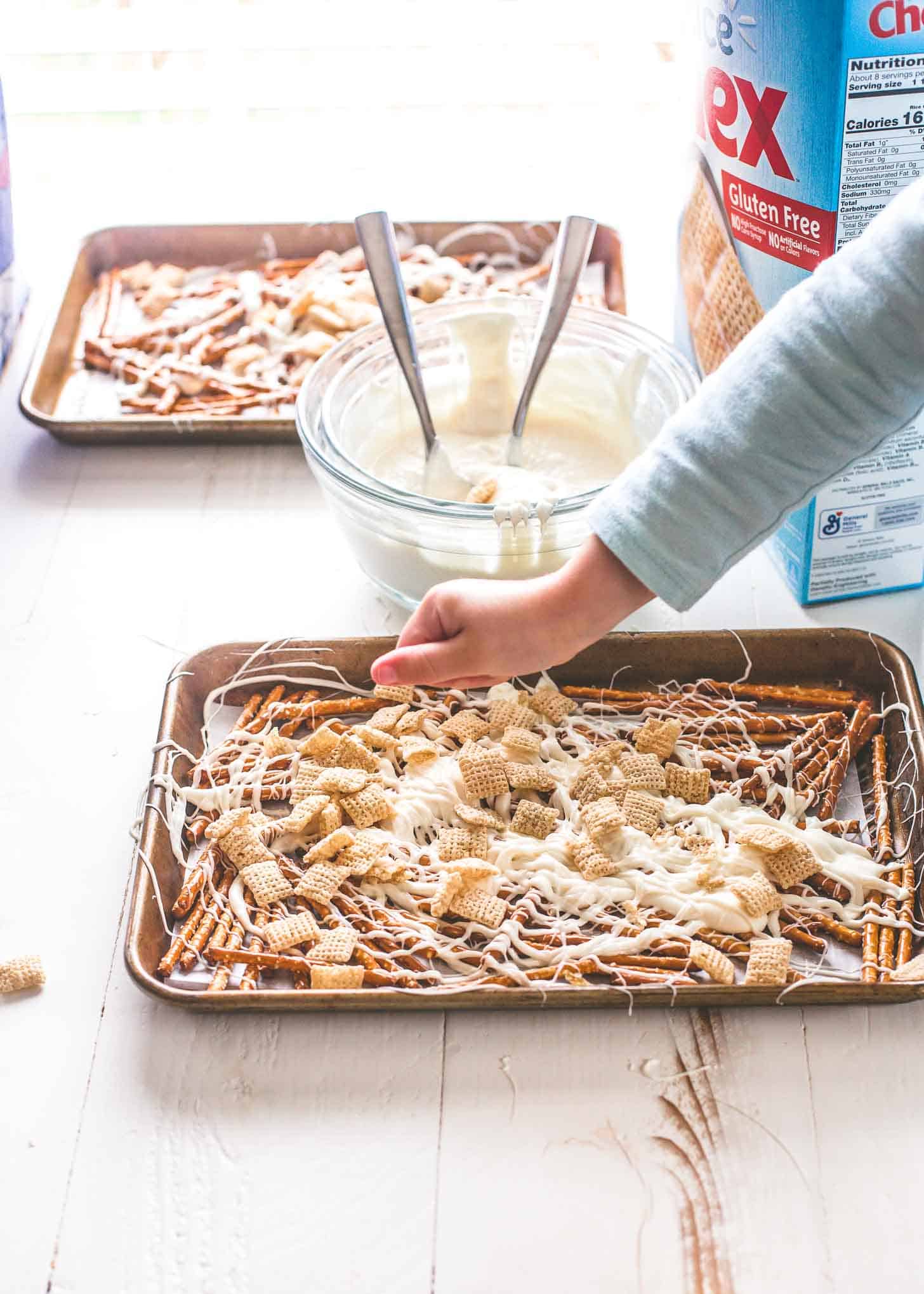 sprinkling chex cereal onto pretzels and almond bark on sheet pans