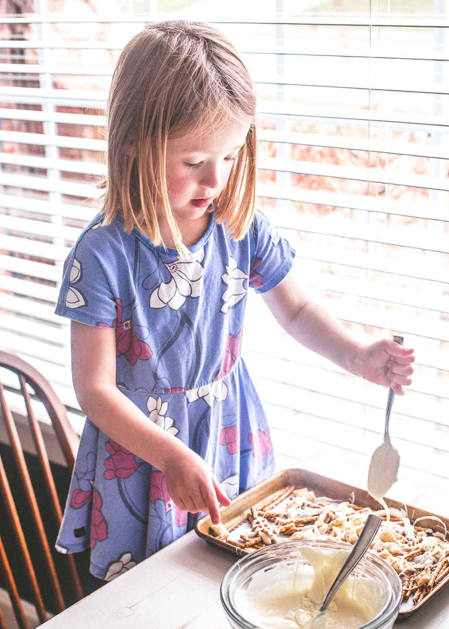a young girl in a purple floral dress drizzles white chocolate over Easter Egg Crunch Bark