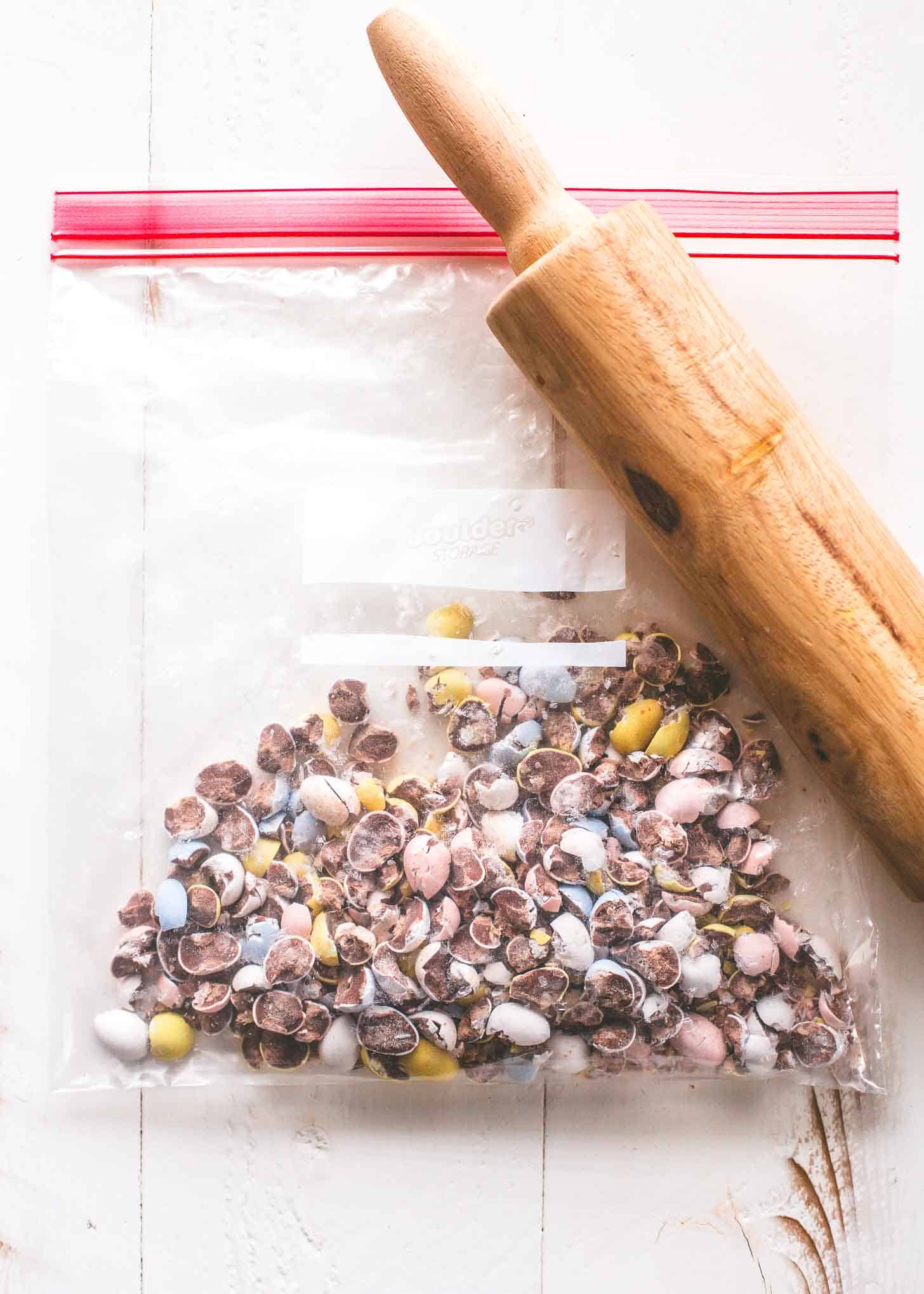 overhead image of mini Easter eggs in a large zippered bag with a rolling pin on a white table
