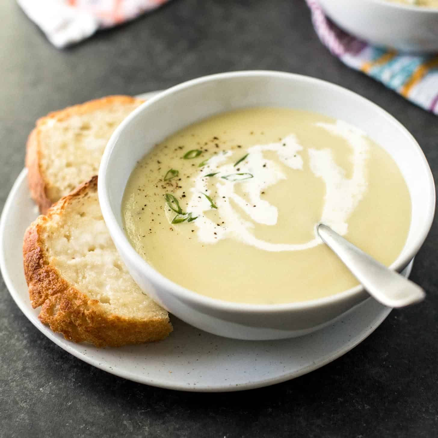 Instant Pot potato leek soup in a white bowl next to sliced crusty bread on a white plate