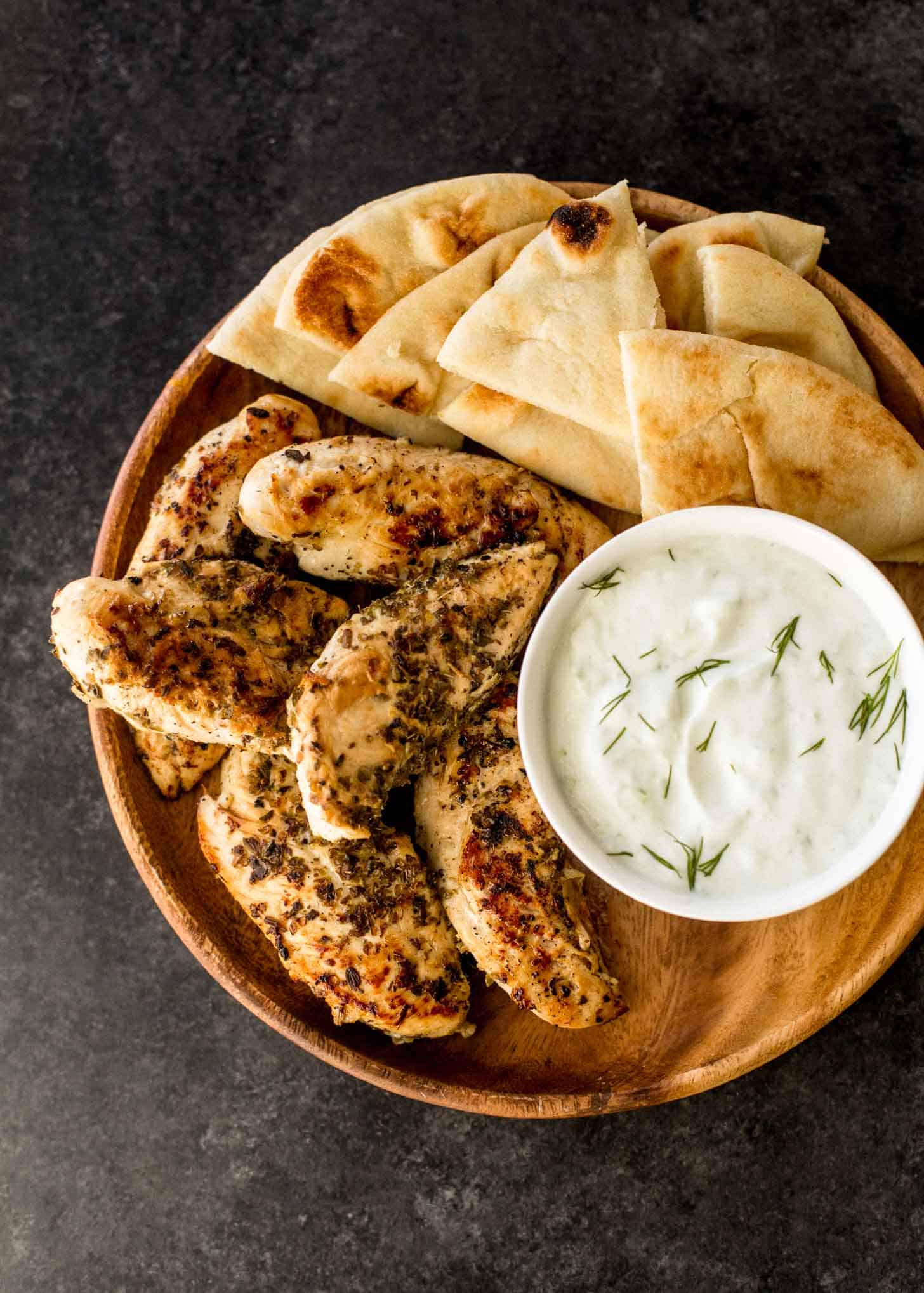 overhead image of chicken with tzatziki and pita bread on a round wooden tray