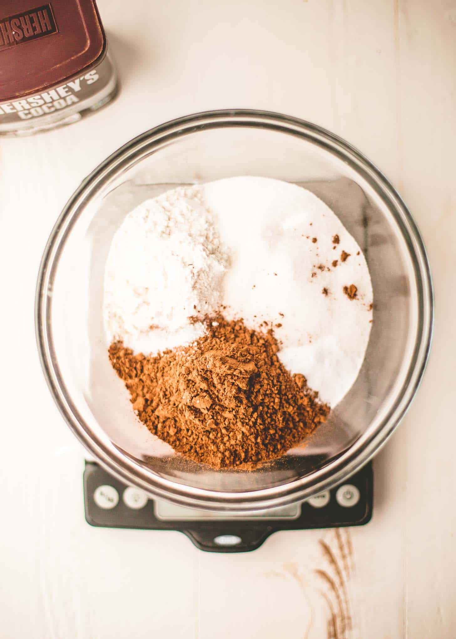 overhead image of dry ingredients for chocolate cake in a bowl on a kitchen scale