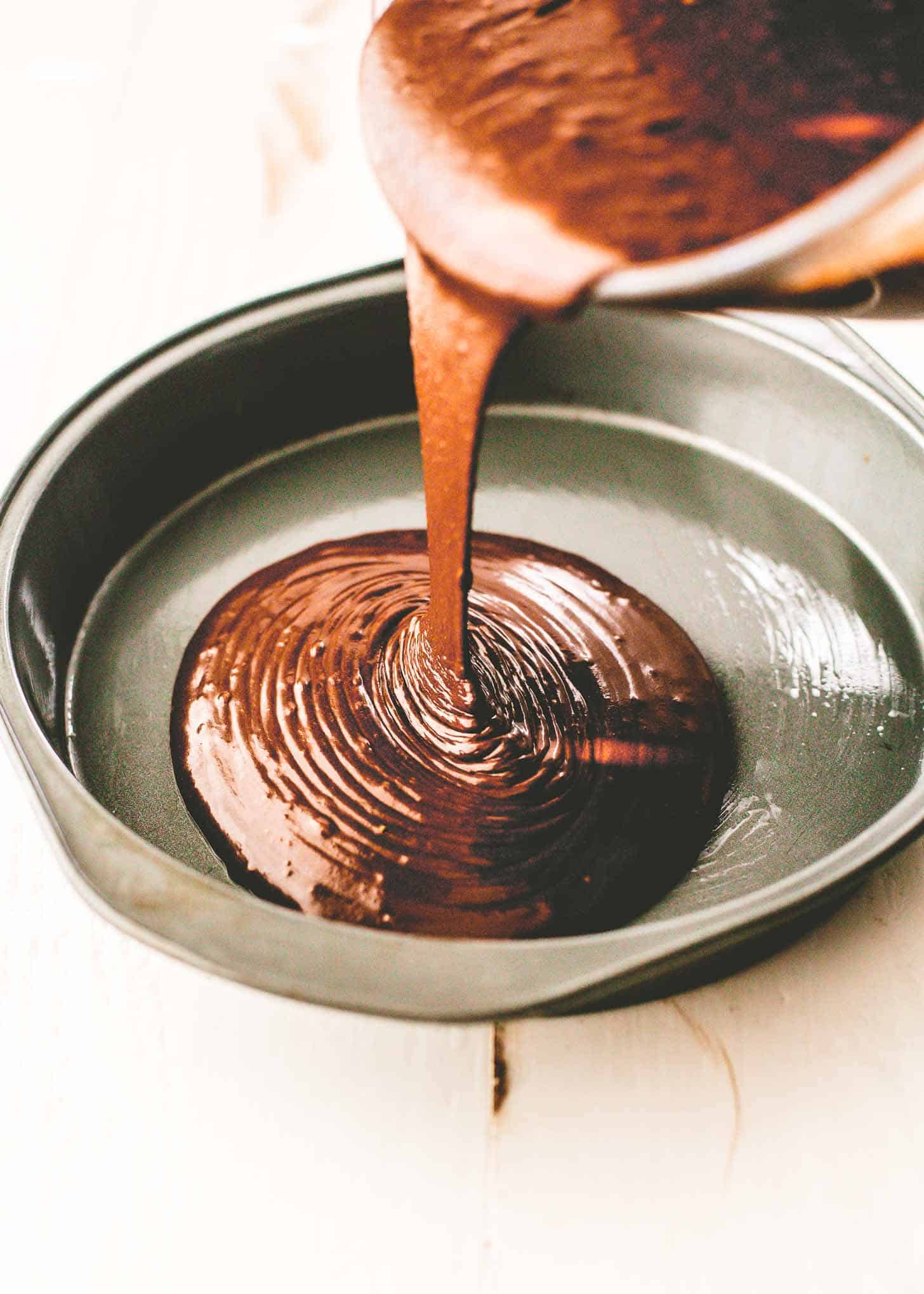 pouring chocolate cake batter into a round cake pan