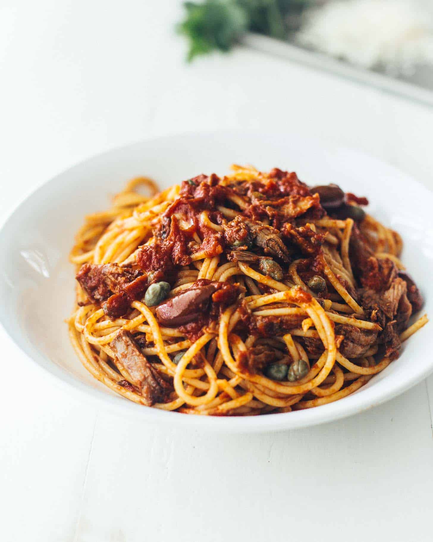 slow cooker beef puttanesca over pasta in a white bowl