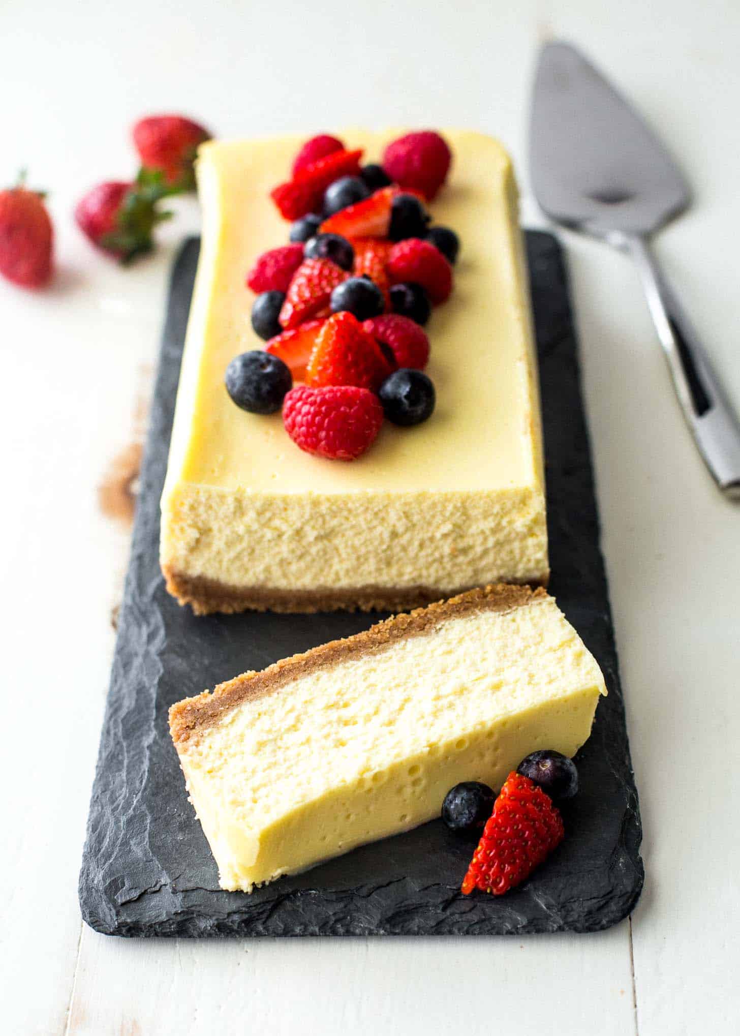 slow cooker classic cheesecake on a grey slate, topped with berries