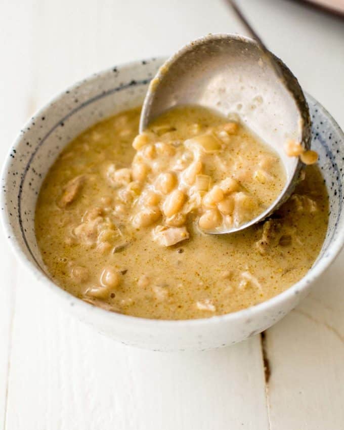 ladling slow cooker white chicken chili into a white enamelware bowl