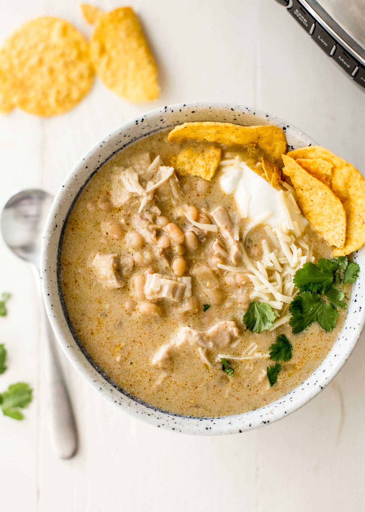 overhead image of slow cooker white chicken chili in a white enamelware bowl with corn chips