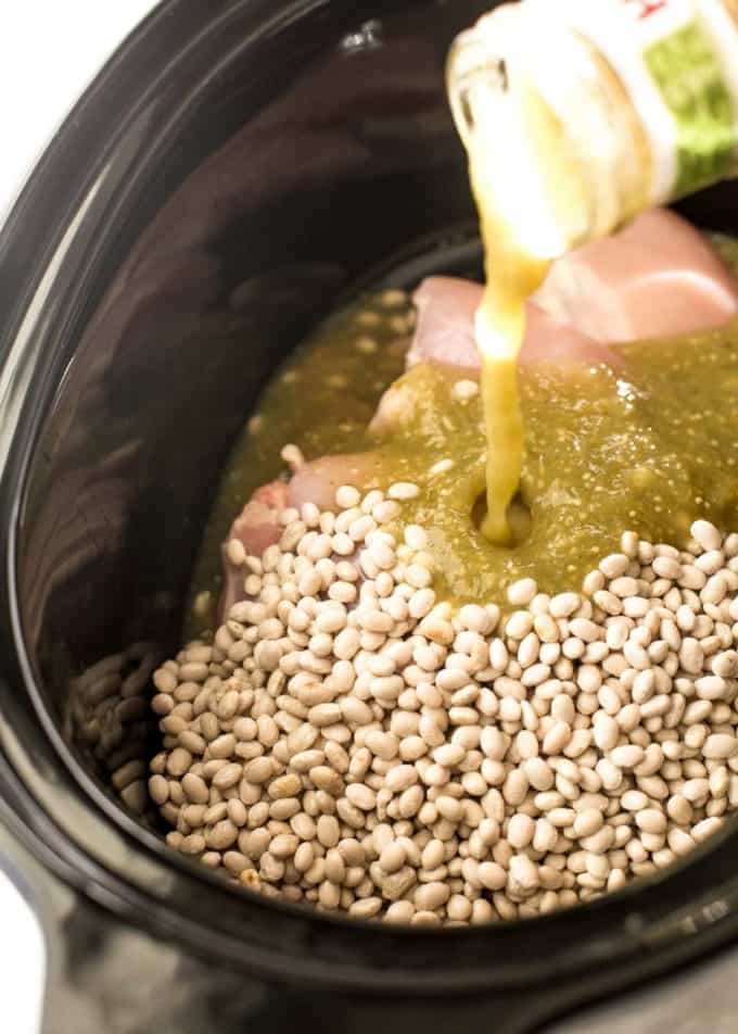 adding salsa verde to white chicken chili ingredients in a slow cooker