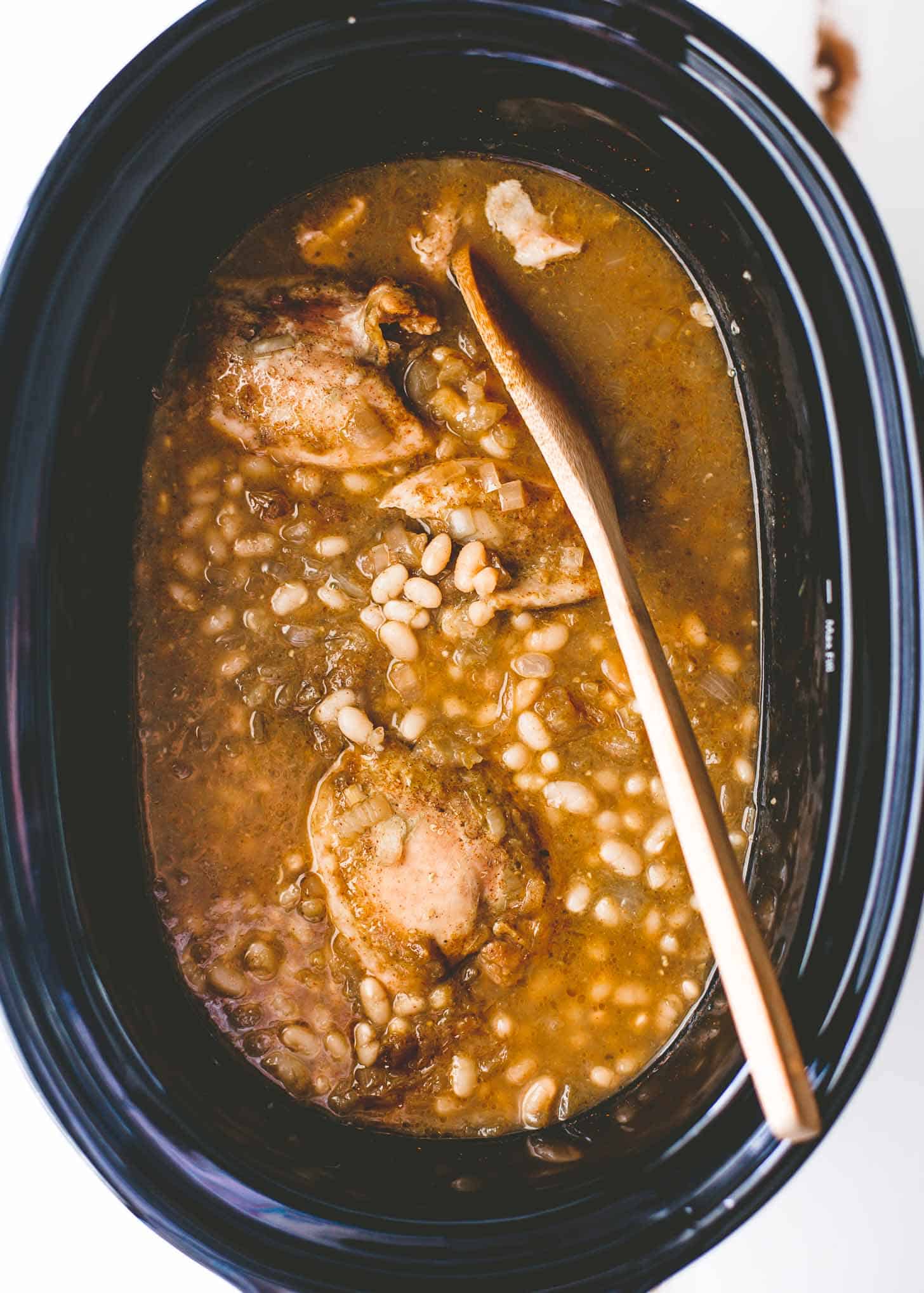 overhead image of white chicken chili in a slow cooker with a wooden spoon