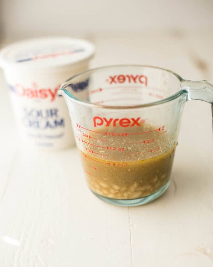 white chicken chili in a clear measuring cup next to sour cream