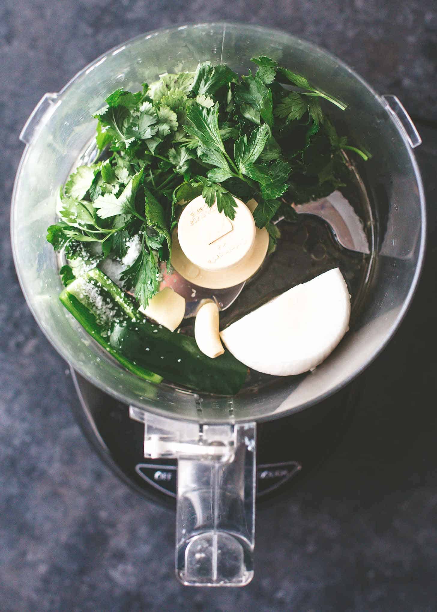 overhead image of herbs, garlic and onions in a food processor