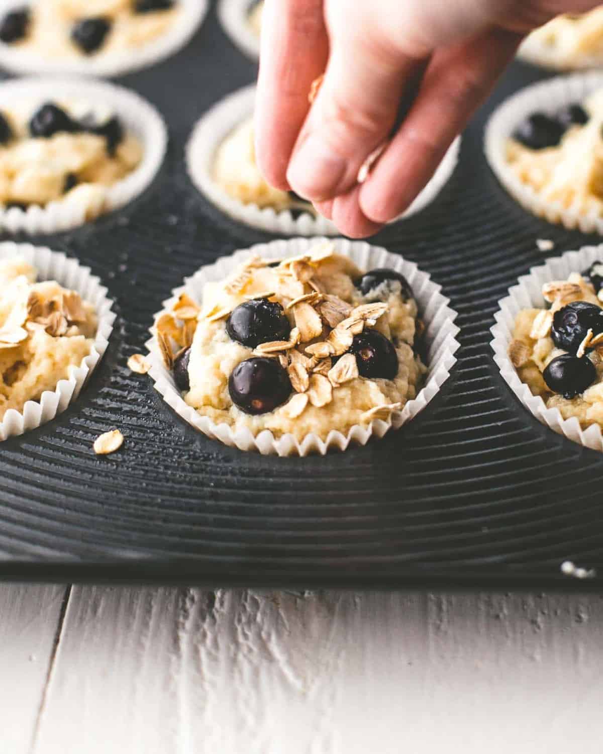 sprinkling oats onto blueberry muffin batter in a muffin tin