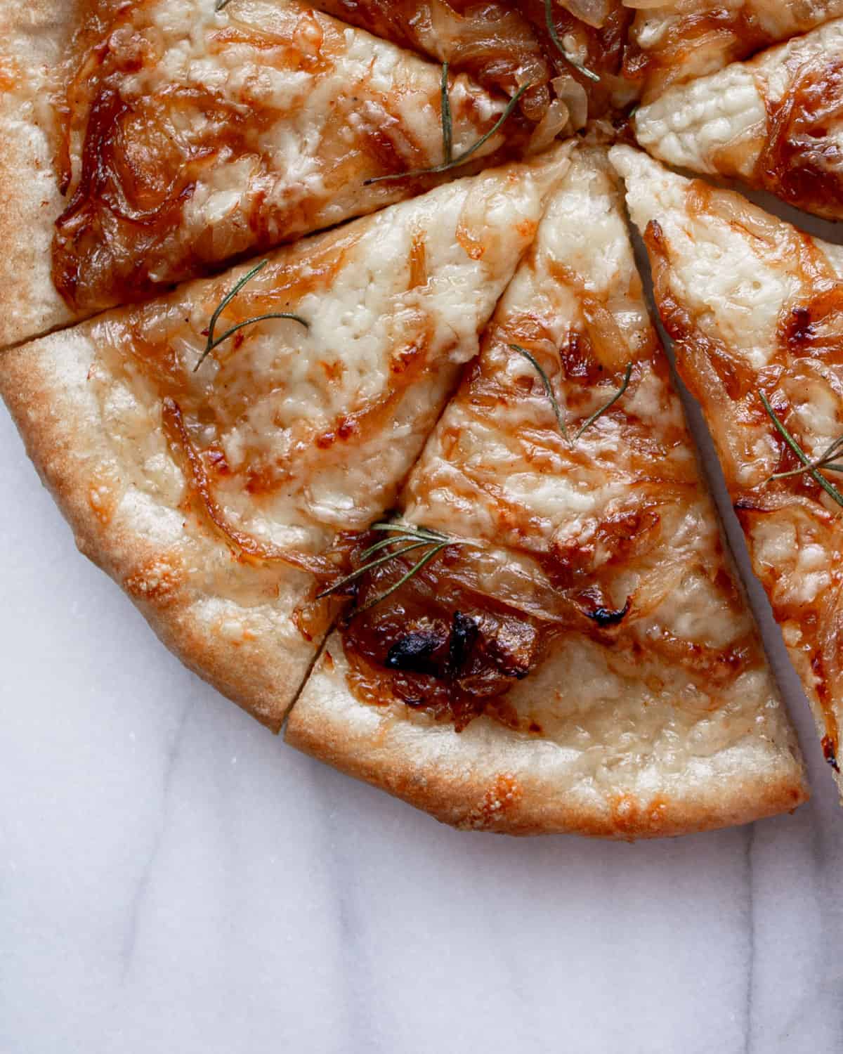 a close shot of two slices of white pizza topped with cheese, caramelized onions, and rosemary