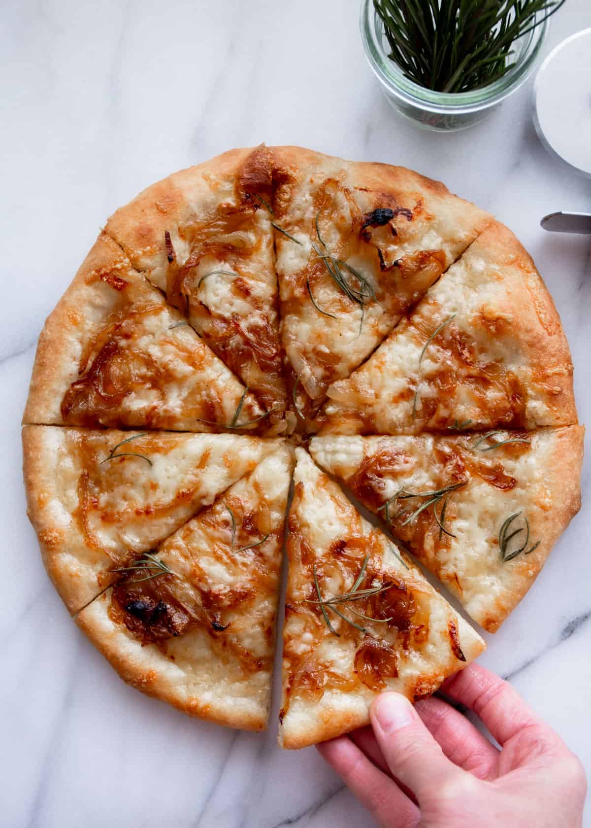 overhead image of caramelized onion pizza in eight slices with a hand reaching for one slice