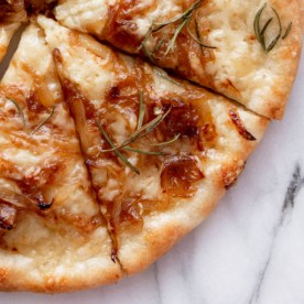 a white pizza sliced on a marble slab and topped with caramelized onions, gruyere cheese, and rosemary sprigs