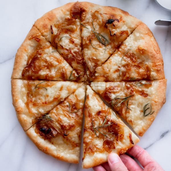 caramelized onion pizza in eight slices with a hand reaching for one slice