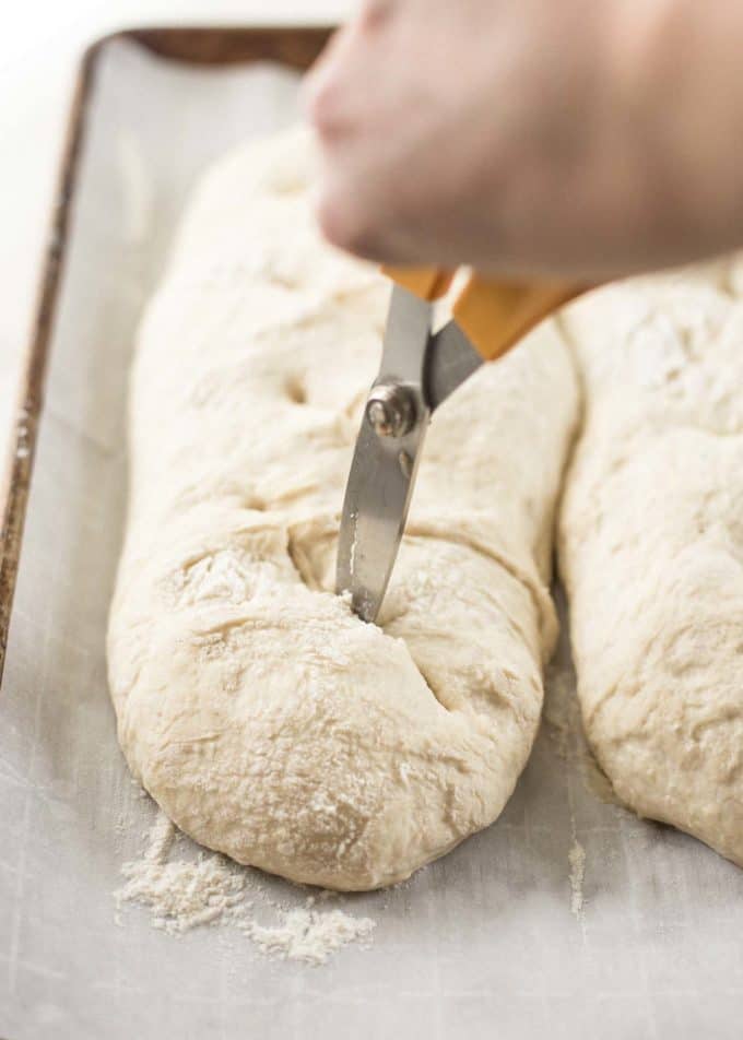 cutting into the tops of no knead french bread with scissors
