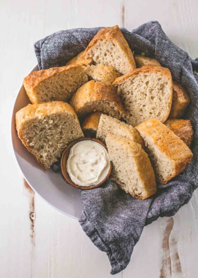 sliced no-knead everyday bread in a bowl with a blue towel with a small ramekin of butter