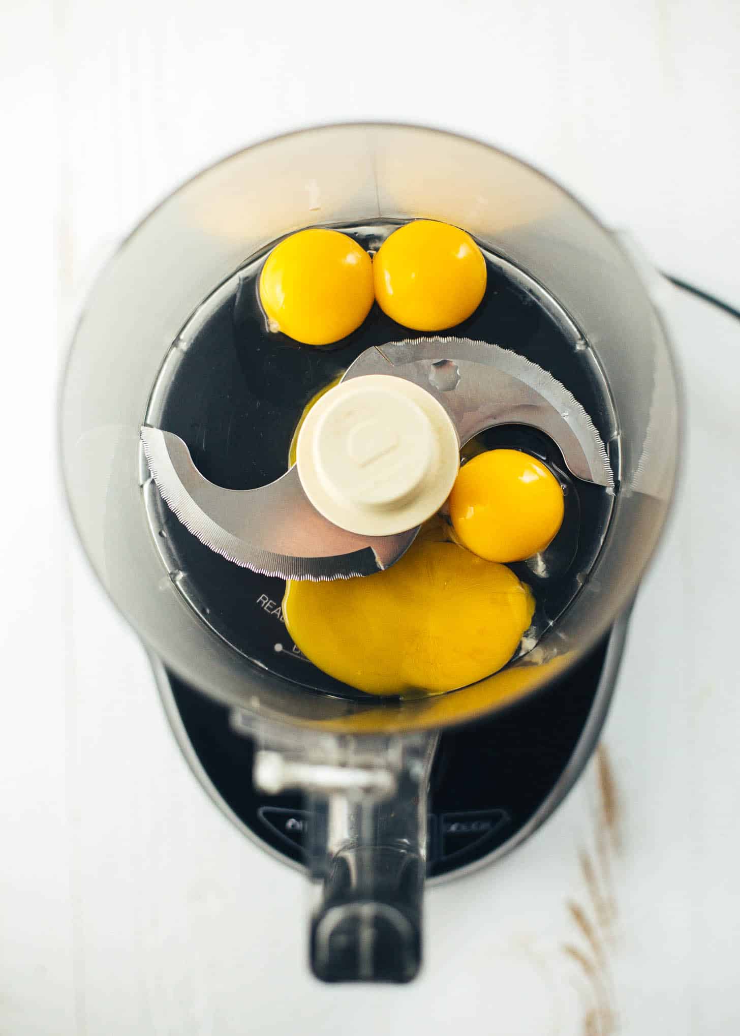 overhead image of egg yolks in the bowl of a food processor