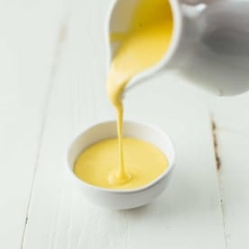 pouring Blender Hollandaise Sauce into a white bowl