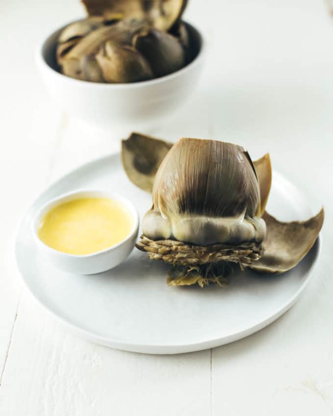Instant Pot Steamed Artichoke on white plate next to a bowl of hollandaise sauce
