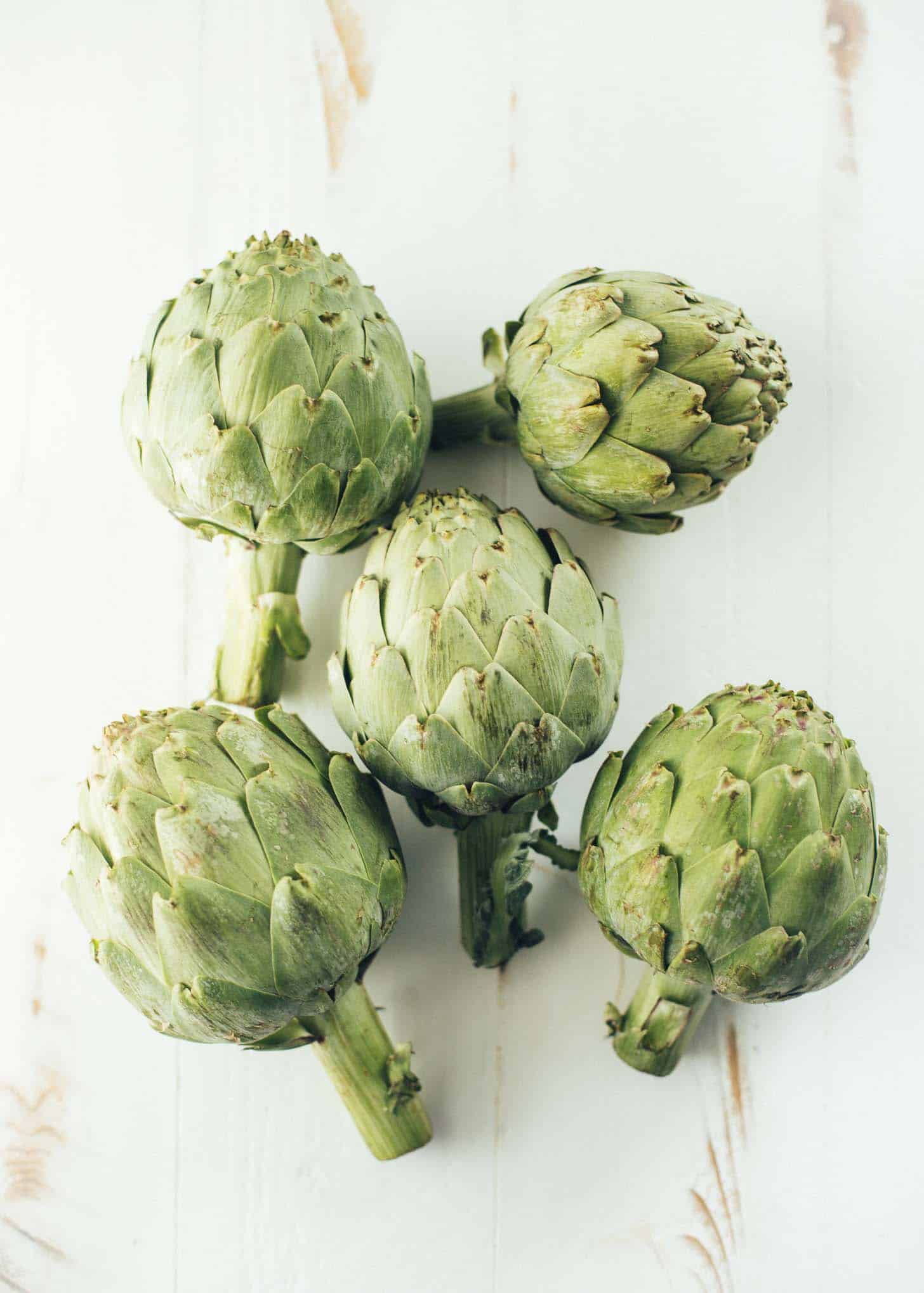 overhead image of 5 whole artichokes lying on a white table