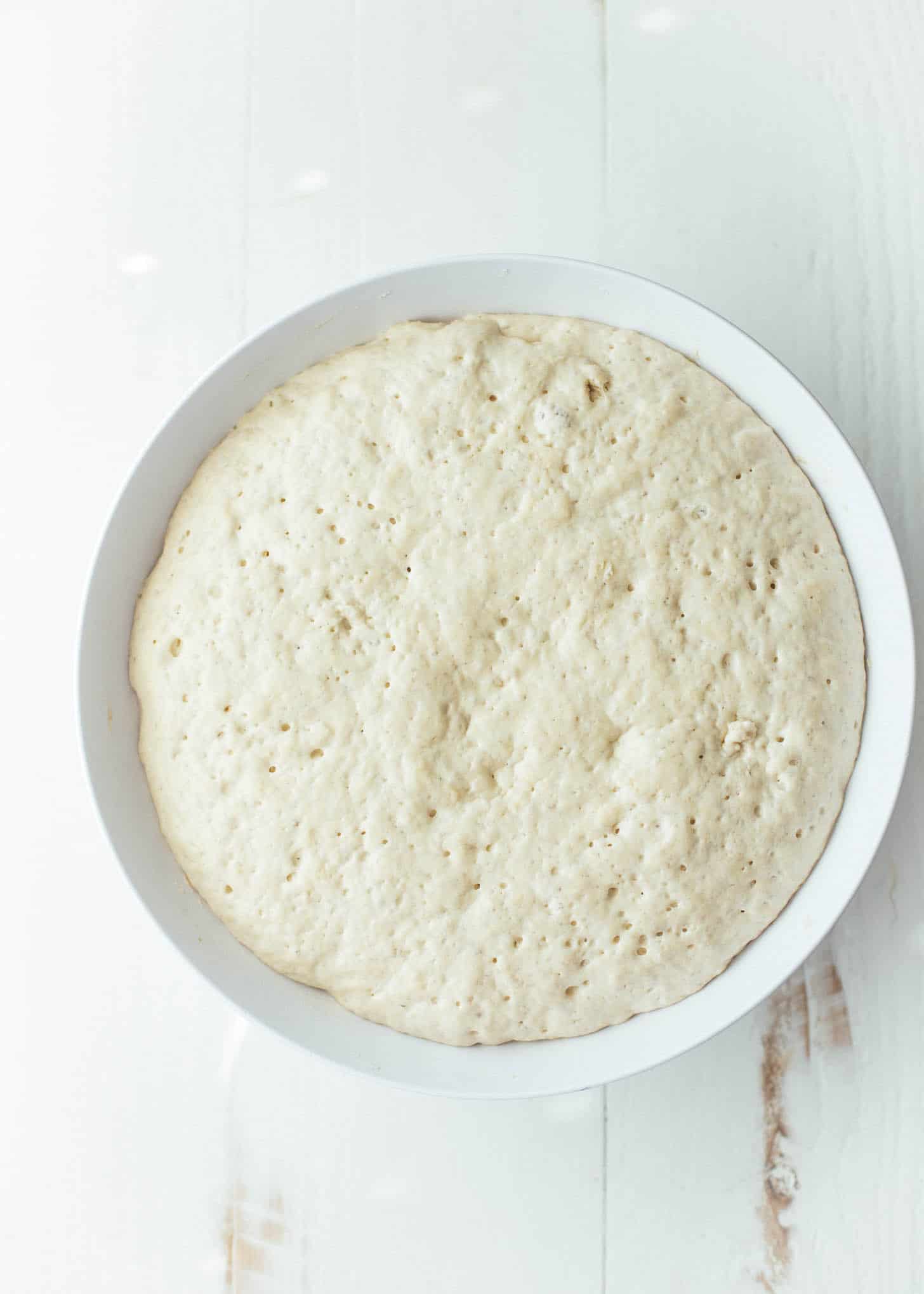 overhead image of focaccia dough after rising in a white bowl