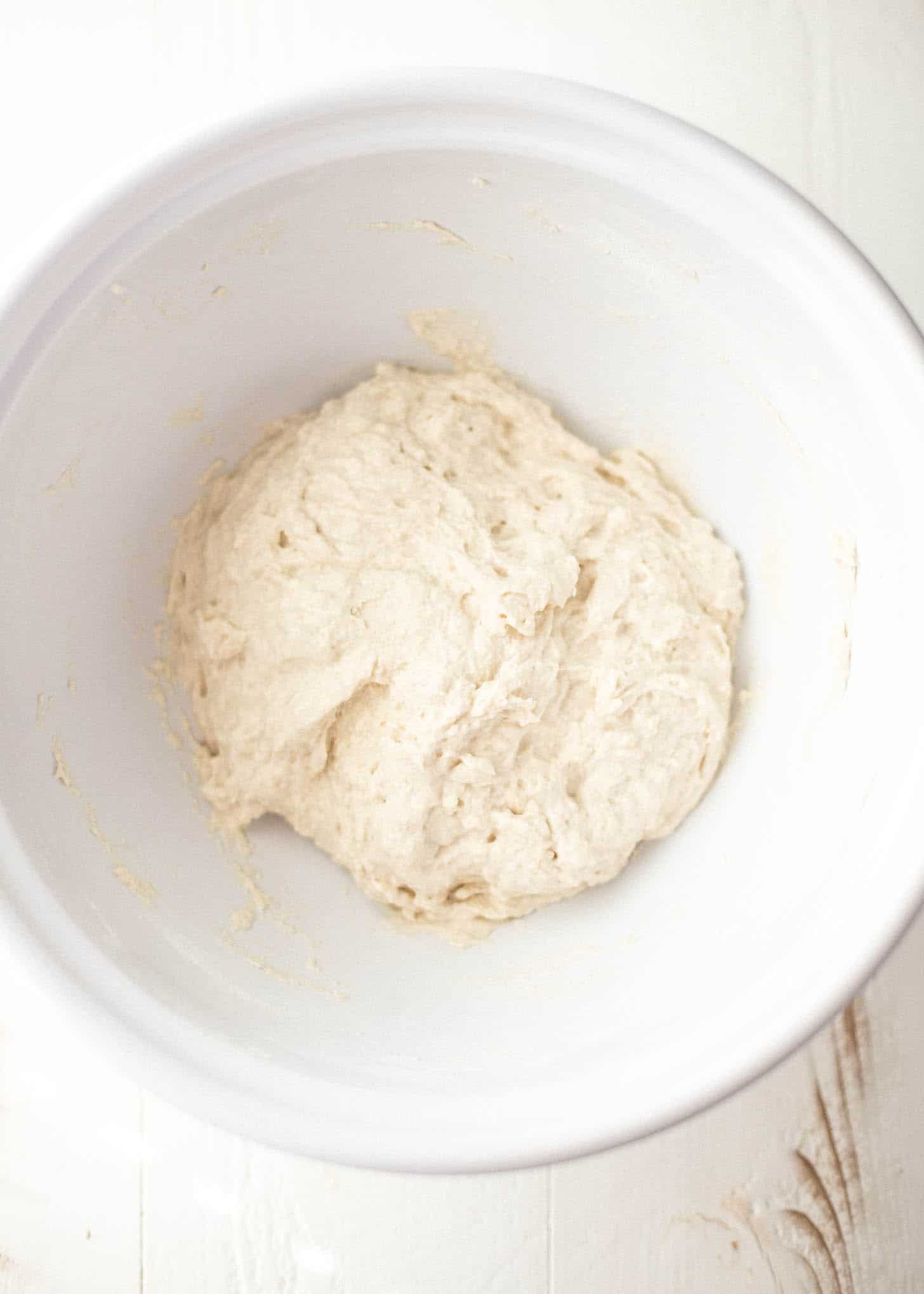 overhead image of pizza dough in a white bowl before rising