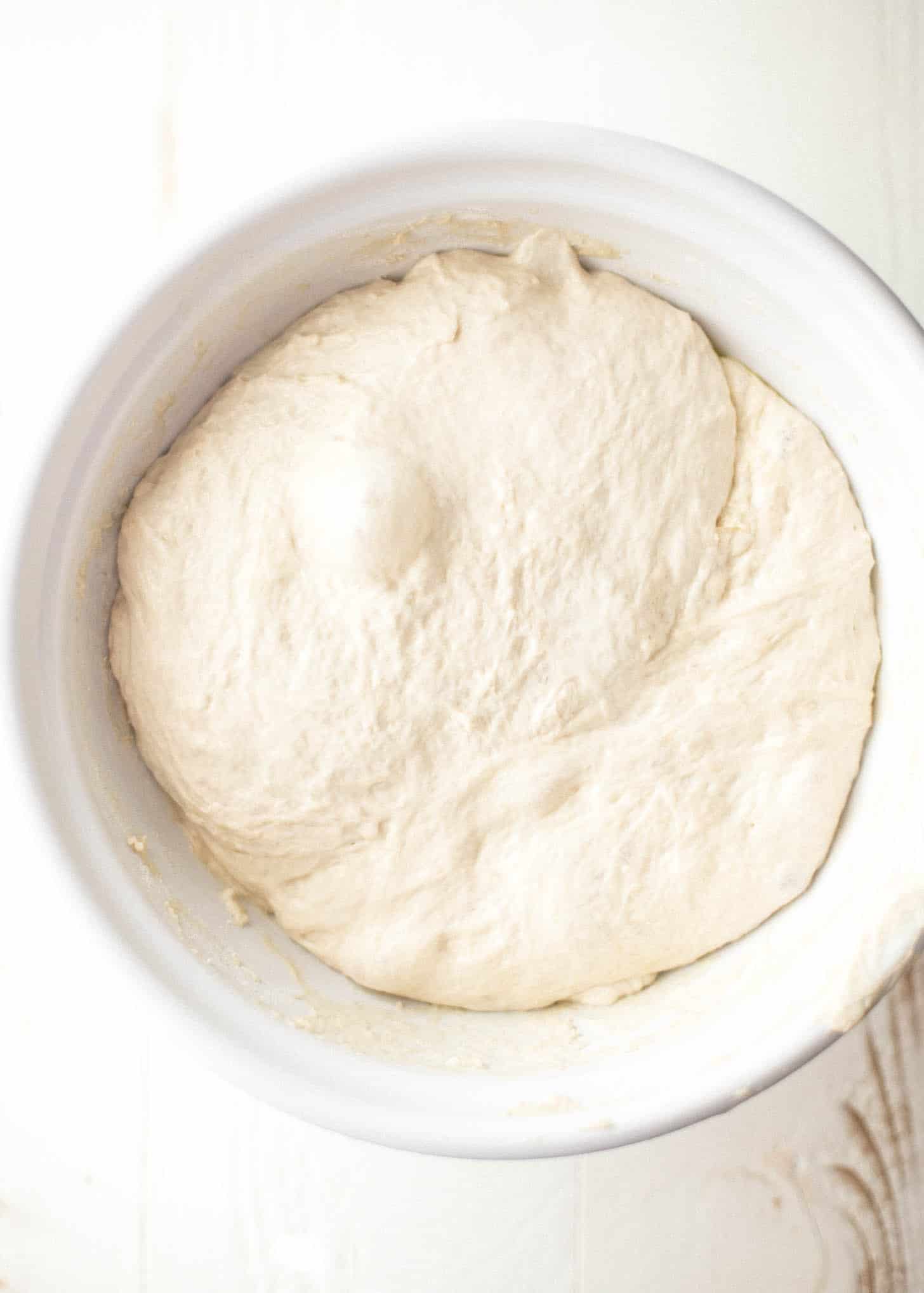 pizza dough in a white bowl after rising