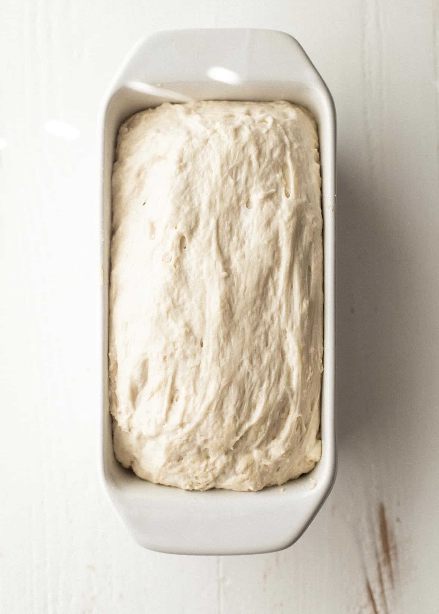 overhead image of No knead sandwich bread dough in a white loaf pan on a white table