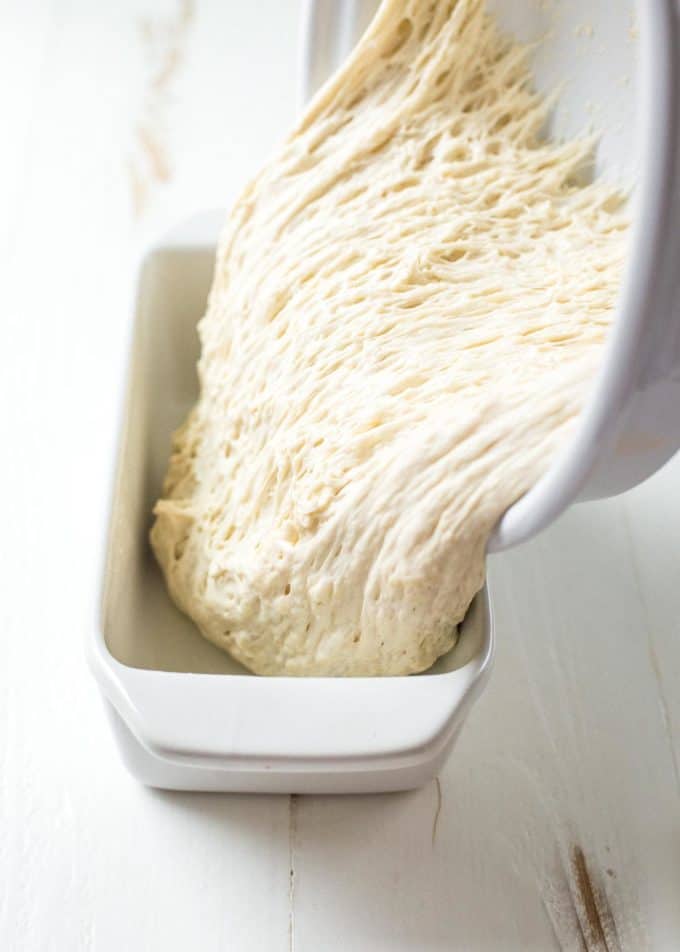 pouring No knead sandwich bread dough into a white loaf pan