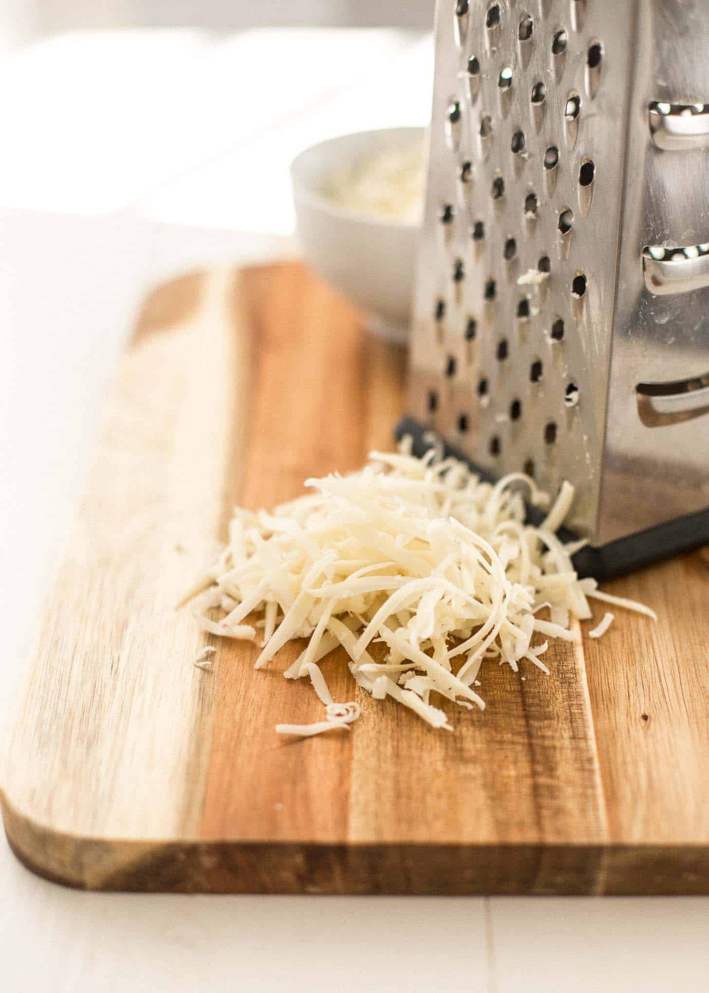 grated gruyere cheese on a cutting board next to a cheese grater